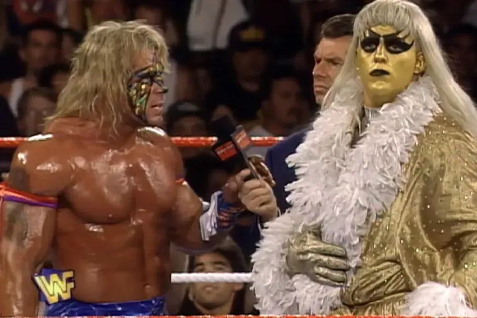 Ultimate Warrior, in "warpaint," confronting an androgynous adversary in gold facepaint, black lipstick, and a gold robe with white feathers. A suited microphone man behind.