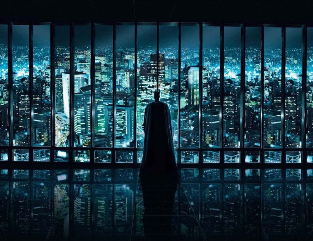 Batman stands before a modern cityscape of glass towers.